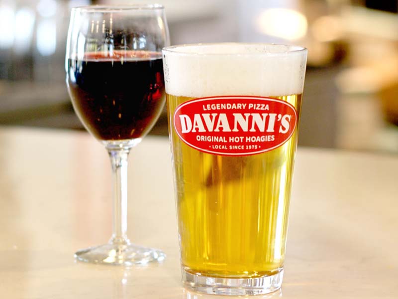 Stemmed glass of red wine and a davanni's logoed glass with a light colored tap beer