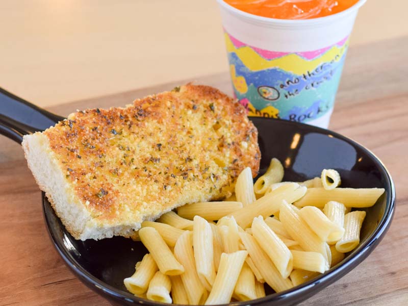 Kids plain pasta served with a side of white toast and a kids sized orange pop. 