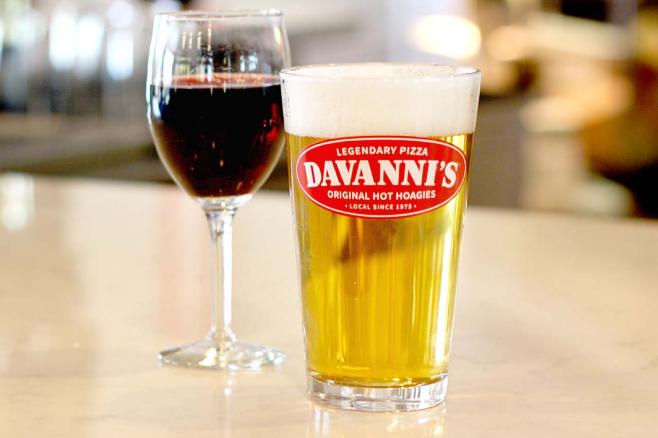 Stemmed glass of red wine and a davanni's logoed glass with a light colored tap beer
