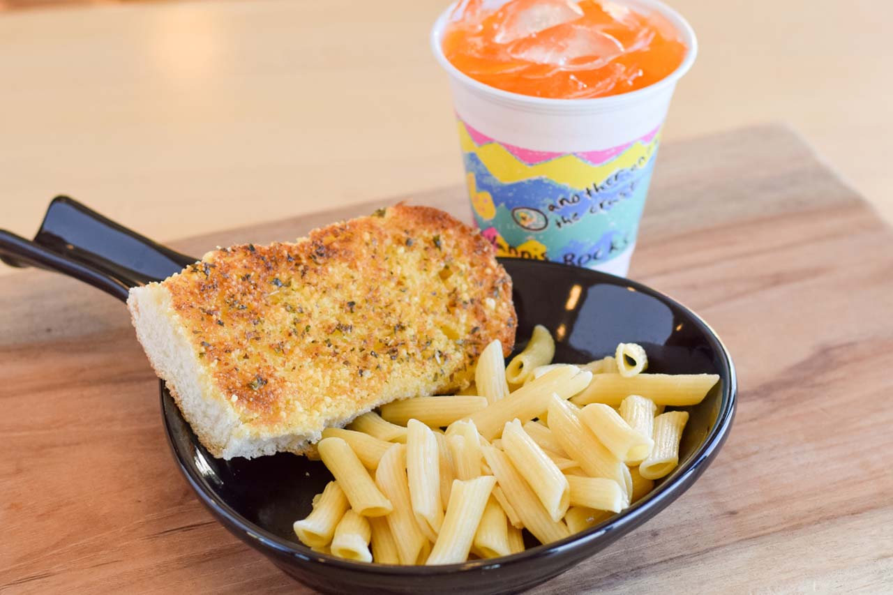 Kids plain pasta served with a side of white toast and a kids sized orange pop.