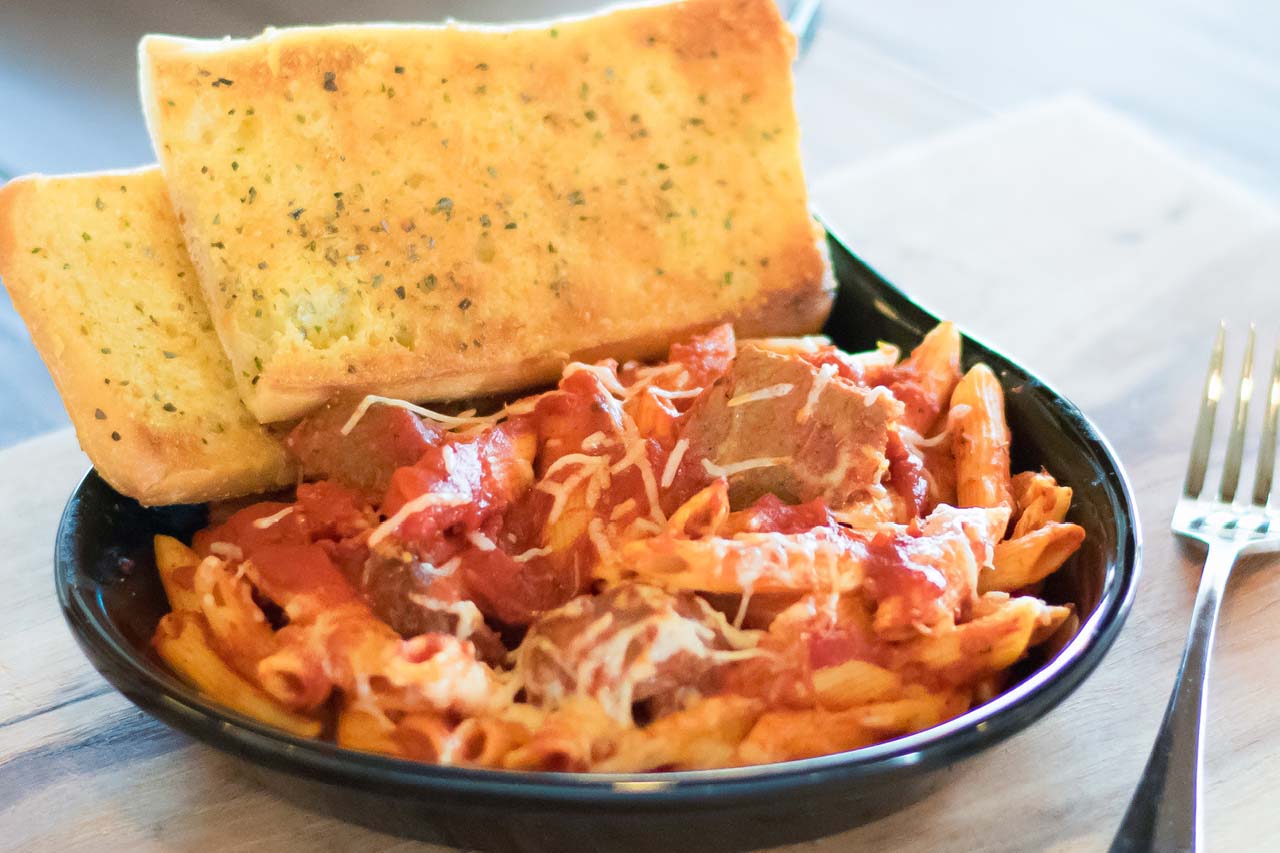 Whole sized penne pasta with red sauce, meatballs, shredded romano cheese, and two pieces of ciabatta garlic toast.
