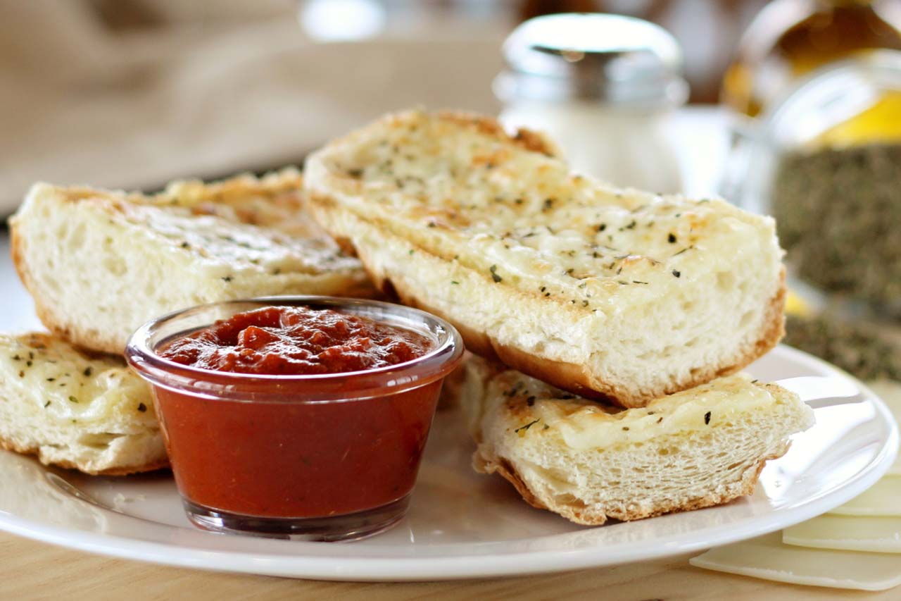 Four piece garlic cheese bread on white bread served with a side of red sauce.