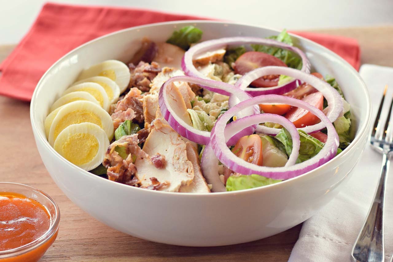 Entree size of the chicken cobb salad includes hard boiled egg, sliced chicken, red onion rings, tomatoes, bacon, and gorgonzola cheese. You choose your own dressing.