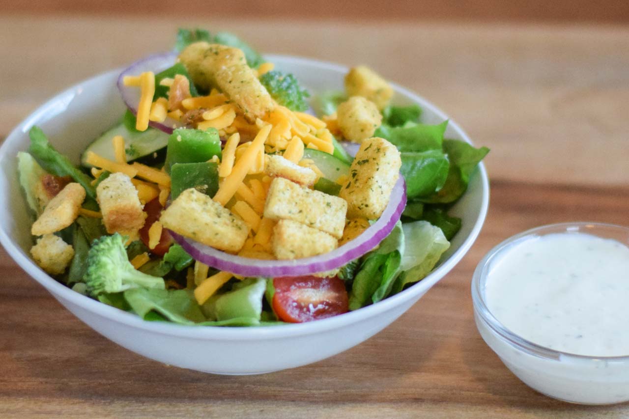 Side sized garden salad with lettuce, cucumbers, red onions, diced green peppers, tomatoes, croutons, cheese, and a dressing of choice.