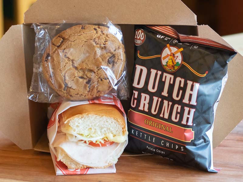 Box lunch with a half cold turkey hoagie, wrapped chocolate chunk cookie, and a bag of original old dutch crunch chips, displayed in a box. 