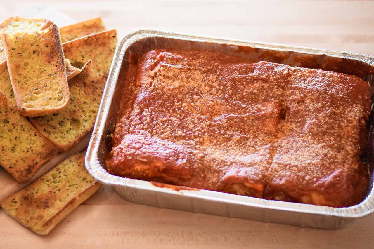 Pan of lasagna topped with red sauce and a romano cheese sprinkle. Served with Ciabatta Garlic Toast.