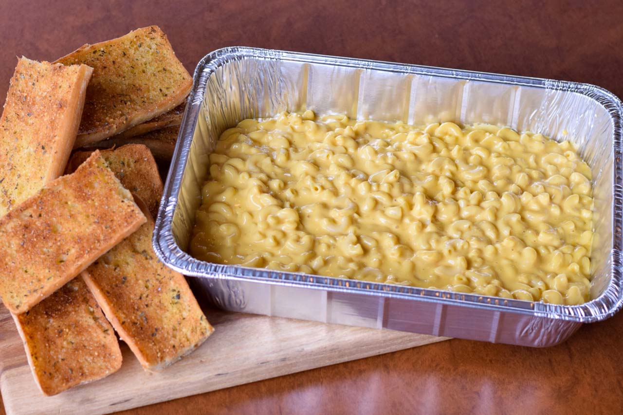 Pan of cheesy mac and cheese noodles served with ciabatta garlic toast.