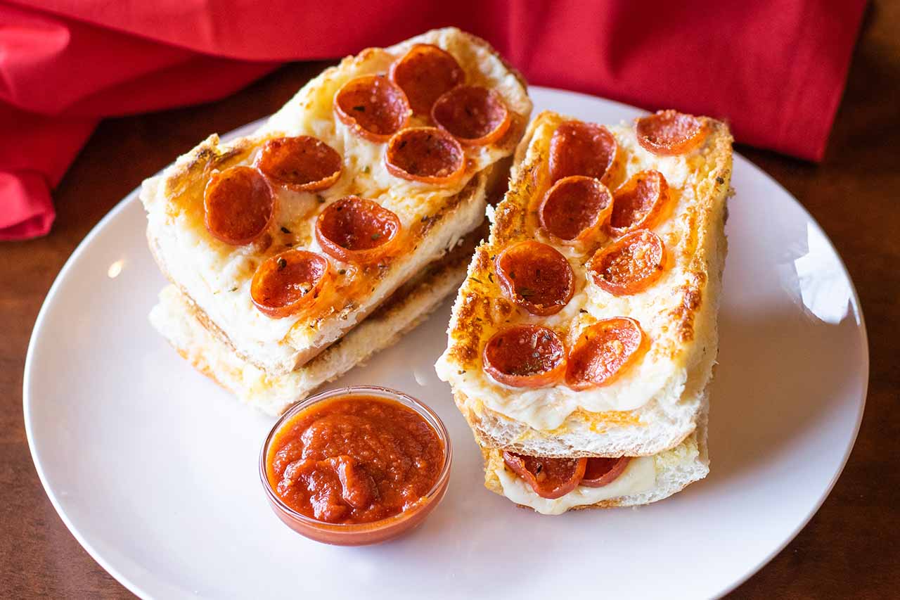 Four piece garlic cheese bread on white bread served with a side of red sauce.
